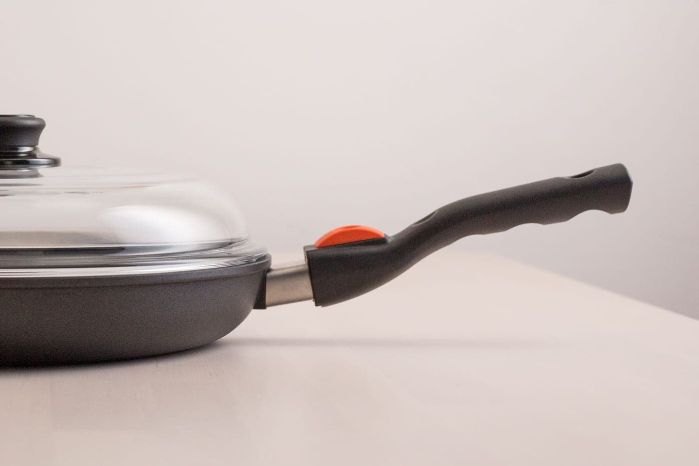 Two frying pans side by side on a plain surface, hard light