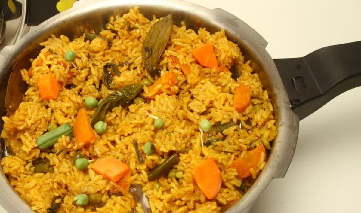 Open stainless steel pressure cooker holding rice and vegetables